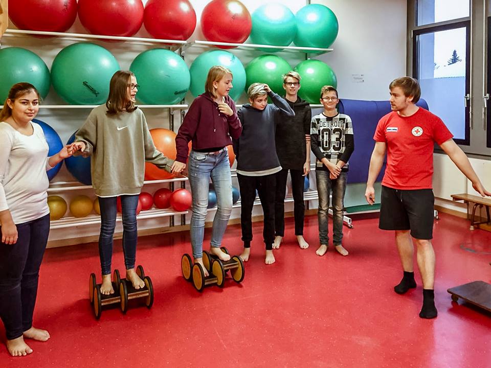 Mehrere Interessierte führen Balance-Übungen durch, während Schüler des Bildungswerkes sie stützen.