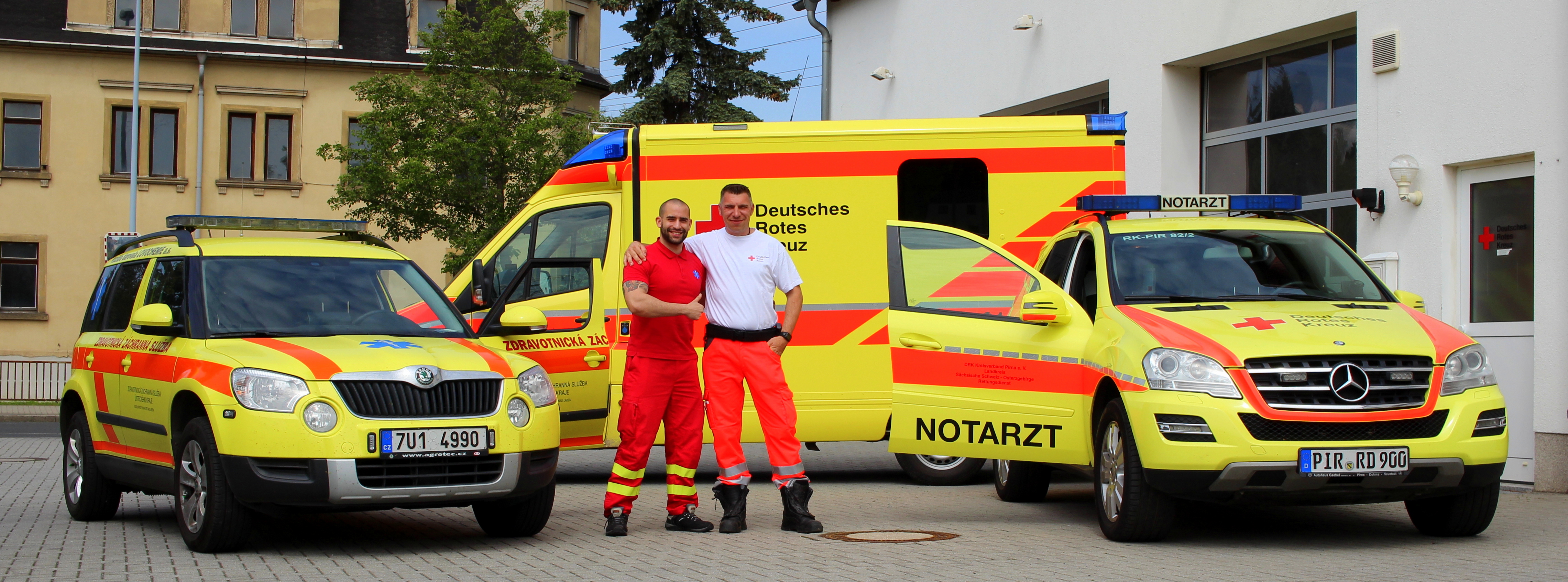 Grenzüberschreitender Rettungsdienst Ein Tschechischer und ein Deutscher Mitarbeiter des Rettungsdienstes stehen Arm in Arm vor ihren Einsatzwagen.