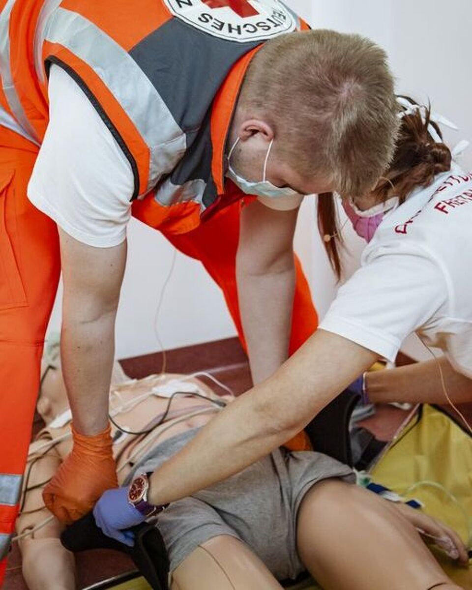 Zwei Auszubildende mit Mundschutz verarzten einen Verletzten.