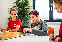 Eine Auszubildende spielt mit einer Frau mit Behinderung ein Brettspiel.