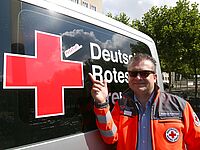 Initiator der Kampagne #status6, Markus Kremser, steht vor dem DRK Einsatzwagen, der mit einem #status6-Aufkleber ausgestattet ist. 