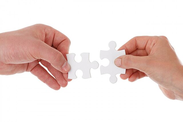 Zwei Hände halten je ein Puzzlestück, die zueinander passen und ein Teil ergeben.