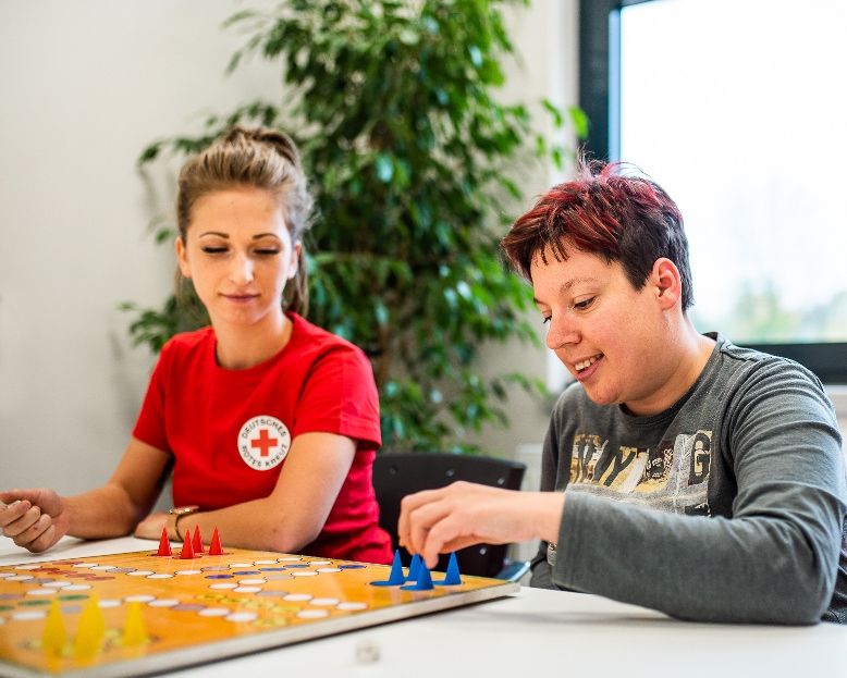 Eine Auszubildende spielt mit einer Frau mit Behinderung ein Brettspiel.