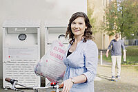 Eine Frau steht am Kleidercontainer und wirft eine Tüte mit aussortierter Kleidung ein.