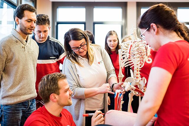 Die Dozentin erklärt den Auszubildenden anhand eines Skeletts den Aufbau und Funktionsweise des menschlichen Körpers.