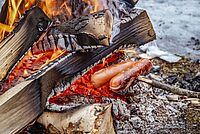 Zwei knackige Würstchen sind auf einem Stock aufgespießt und werden über einem Feuer gegrillt.