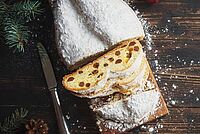 Ein aufgeschnittener Rosinenstollen liegt auf einem Holzbrett. Er wurde mit einer großen Menge Puderzucker verziert.
