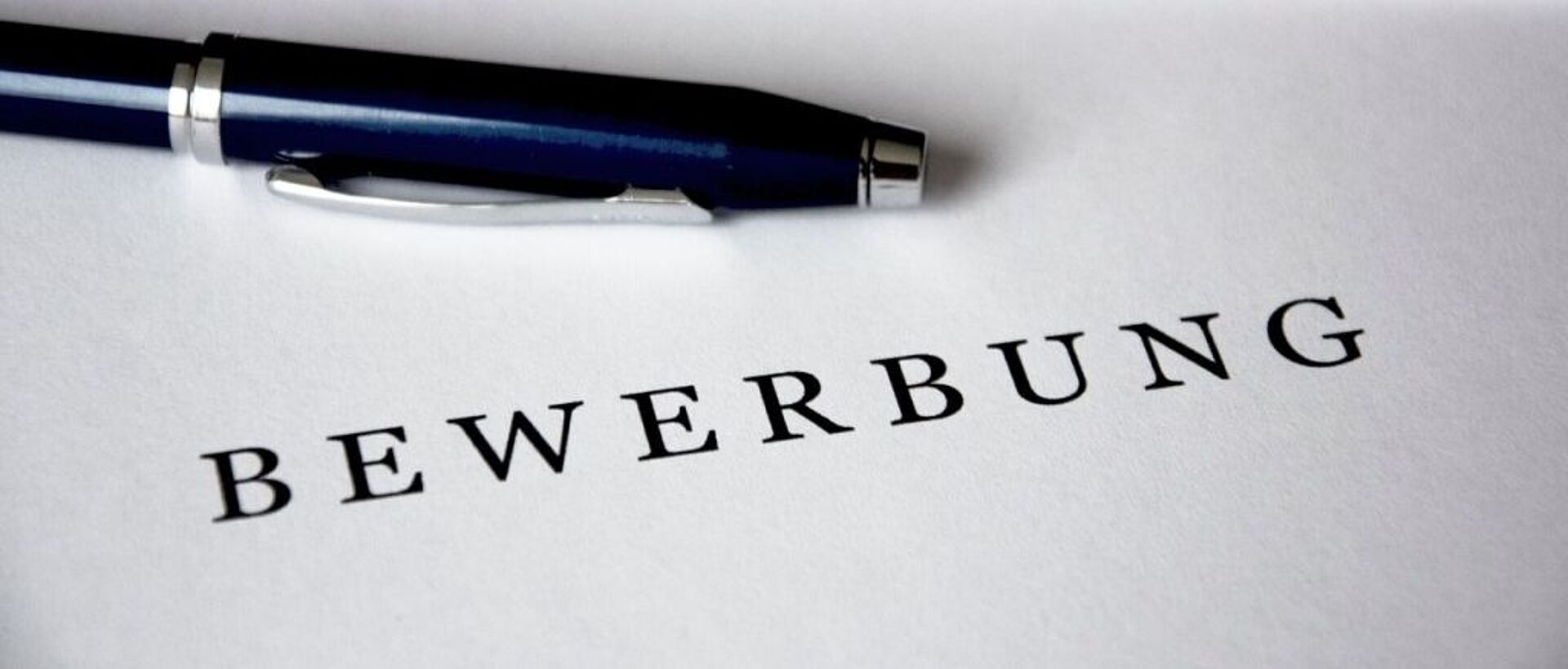 Auf einem Zettel steht "Bewerbung" und ein Stift liegt daneben.