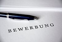 Auf einem Zettel steht "Bewerbung" und ein Stift liegt daneben.