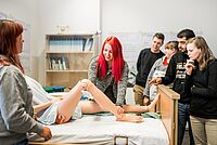 Die Dozentin zeigt den Auszubildenden den richtigen Umgang mit einer pflegebedürftigen Person am Beispiel einer Lehr-Puppe.