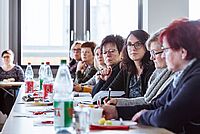 Die Teilnehmerinnen sitzen an einer langen Tischreihe und schauen interessiert zur redenden Person.
